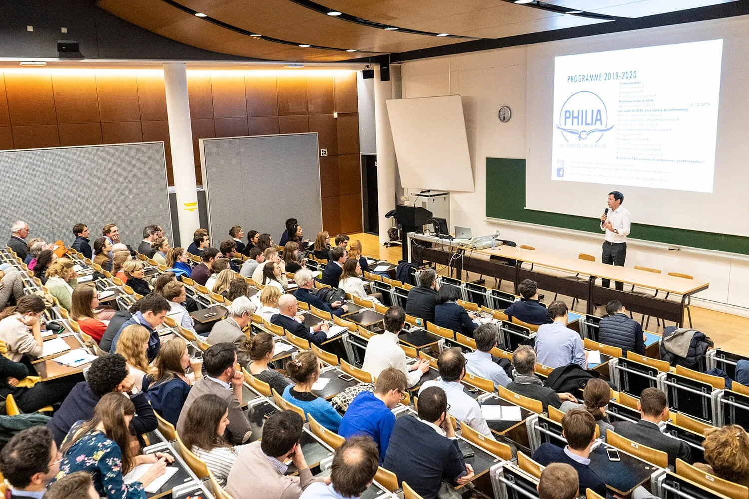 Public assis dans un amphithéâtre face à un intervenant et à un écran
