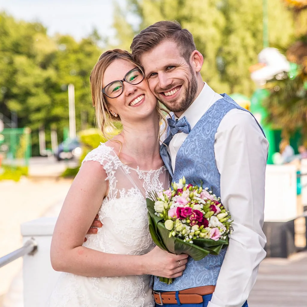 Couple de mariés souriant en extérieur, la mariée tenant un bouquet