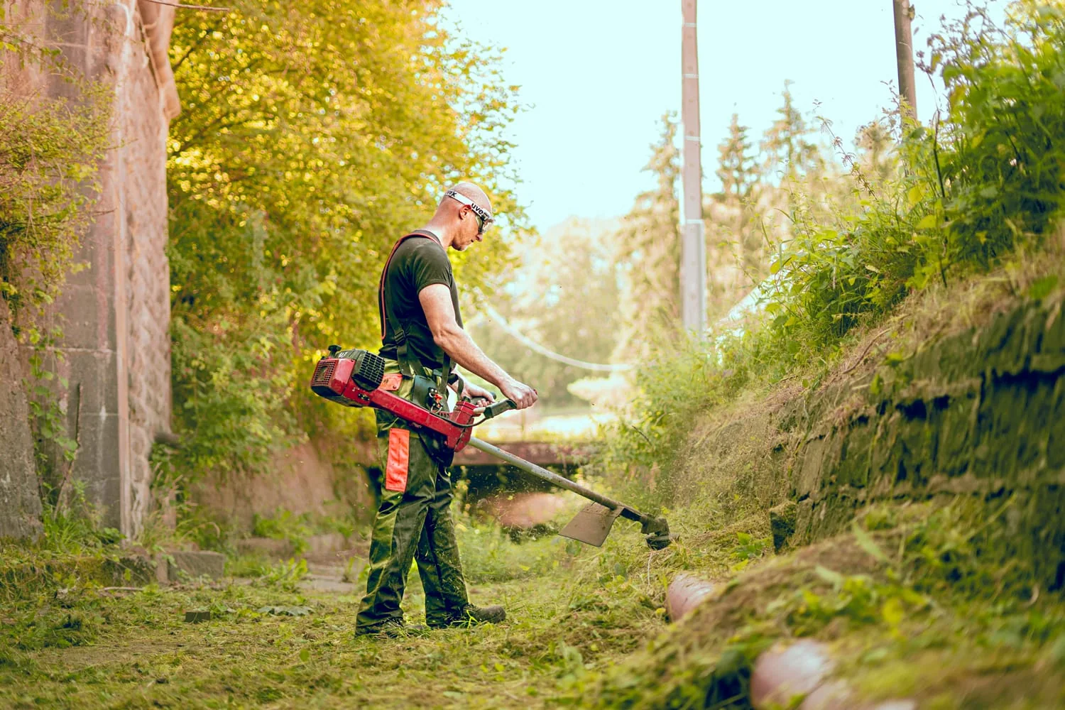 Jardinier utilisant une débroussailleuse sur un terrain arboré