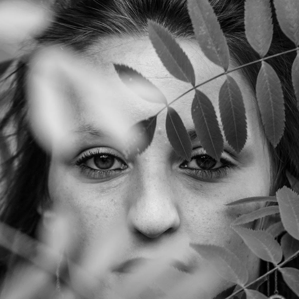 Portrait en noir et blanc d’une femme derrière des feuilles